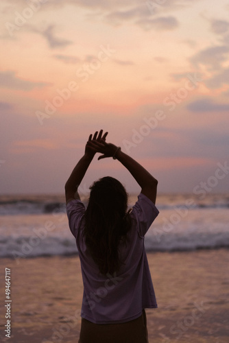 A young beautiful woman on the shore of the ocean at sunset enjoys freedom, place, time. View from the back. flowing clothes.