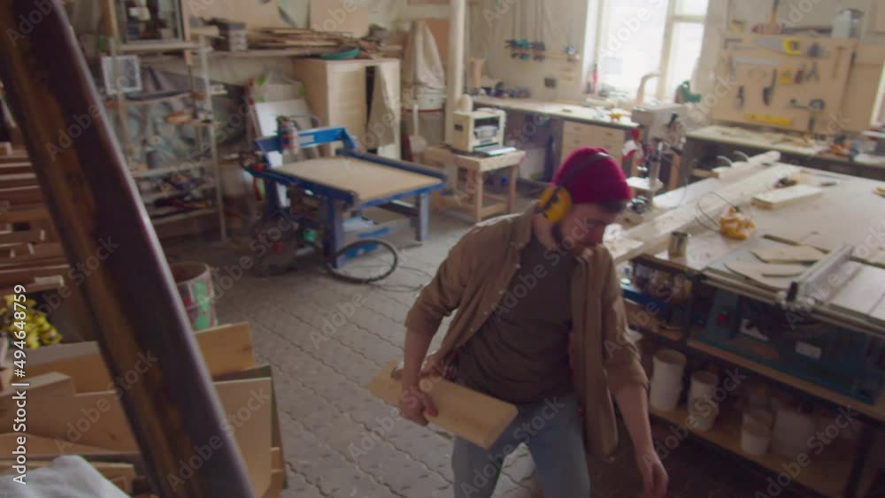 High angle shot of woodworker in safety earmuffs taking plank from shelf in carpentry workshop and then planing it on router table High angle shot of woodworker in safety earmuffs taking plank from shelf in carpentry workshop and then planing it on router table