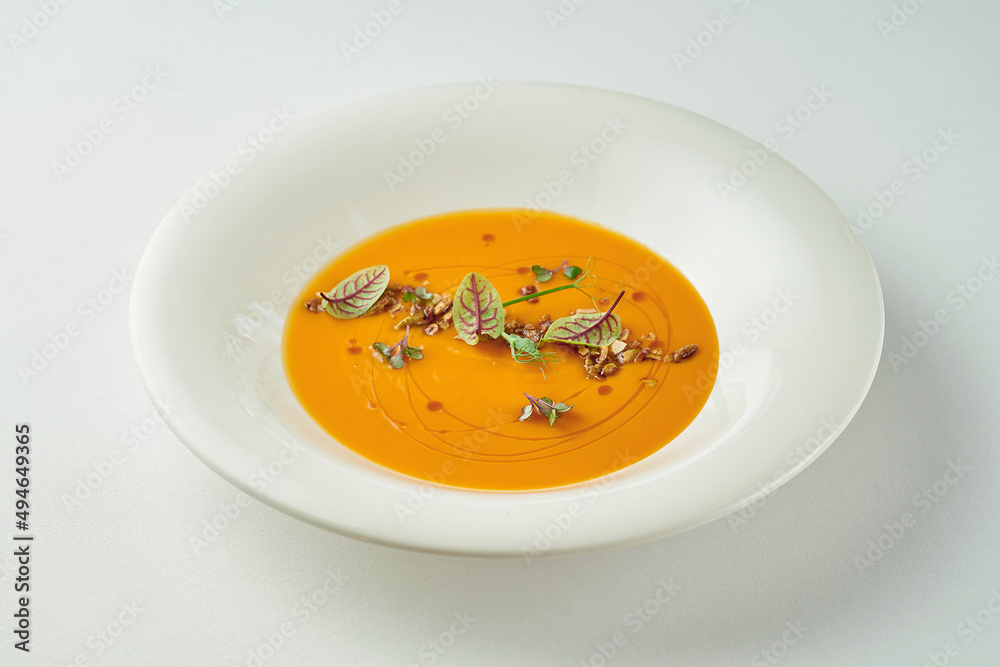 Pumpkin cream soup in a white plate on a white tablecloth Pumpkin cream soup in a white plate on a white tablecloth