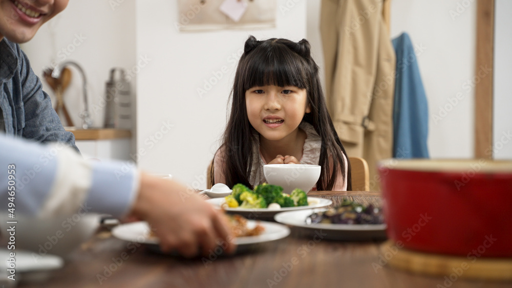 selective focus of hungry Asian girl looking at delicious food her mother is serving on table during dinner time at home
