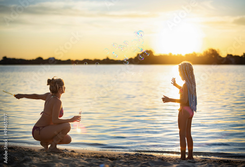 Mom plays with her daughter blowing bubbles on the shore near the lake