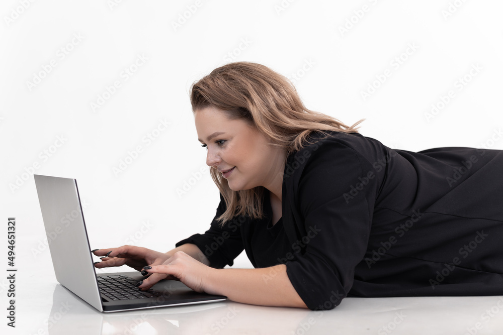 Portrait of beautiful middle-aged fat plus-size woman wearing black cardigan, lying on white floor, typing on laptop. Portrait of beautiful middle-aged fat plus-size woman wearing black cardigan, lying on white floor, typing on laptop.