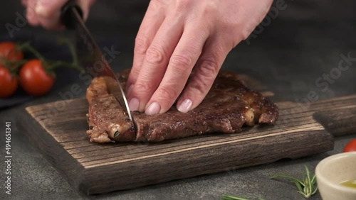 Chef with Knife Cuts of Grilled Beef Steak on Rustic Cutting Board on Gray Background. Concept of Delicious Meat Food. Juicy Sliced Rib Eye Steak with Salt. 