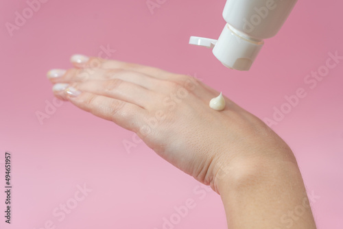 Young hands squeezing cream from tube on pink background. For beauty or medicine products
