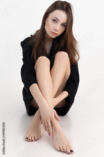 Portrait of young beauteous woman with long dark hair professional make-up wear black coat sitting bending perfect legs.