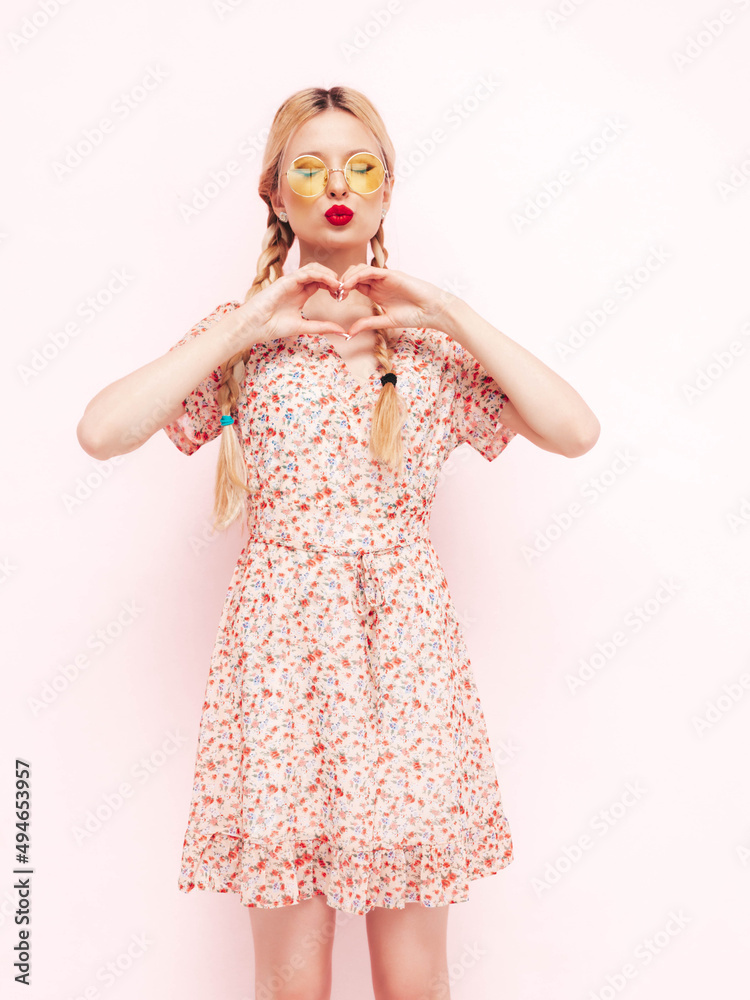 Young beautiful smiling female in trendy summer red dress. Sexy carefree blond woman posing near wall in studio. Positive model having fun. Cheerful and happy in sunglasses. Makes heart sign Young beautiful smiling female in trendy summer red dress. Sexy carefree blond woman posing near wall in studio. Positive model having fun. Cheerful and happy in sunglasses. Makes heart sign