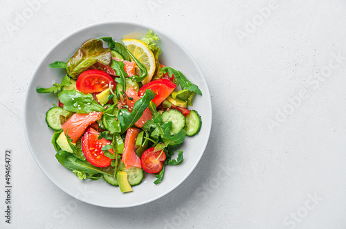 Salad with salmon and fresh vegetables on a light gray background.