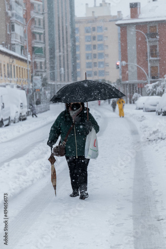 A woman with umbrella with a bag in her hand walking in a snow day with buildings and a cars background © ruben