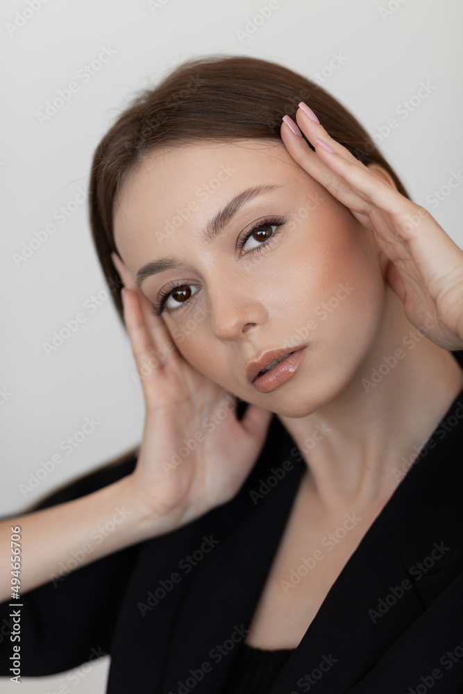 Portrait of young beautiful woman model with long dark hair, make-up in black blazer touching head with hands, posing. Portrait of young beautiful woman model with long dark hair, make-up in black blazer touching head with hands, posing.