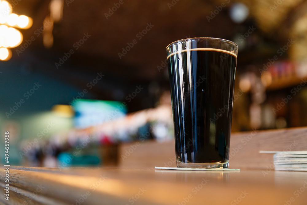 A mug of dark beer on a wooden bar, close-up, with a blurred background.