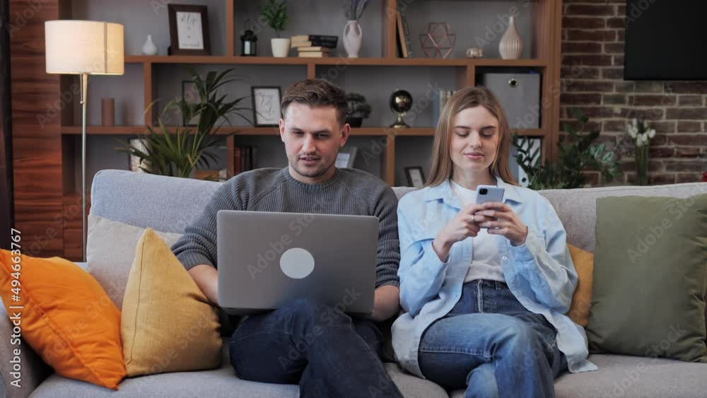 Young Couple of Married People Using Modern Technology Laptop and mobile phone in Living Room. Husband and Wife Communicating via Internet, Social Media Ignore Each Other. Addiction to Gadgets. Young Couple of Married People Using Modern Technology Laptop and mobile phone in Living Room. Husband and Wife Communicating via Internet, Social Media Ignore Each Other. Addiction to Gadgets.