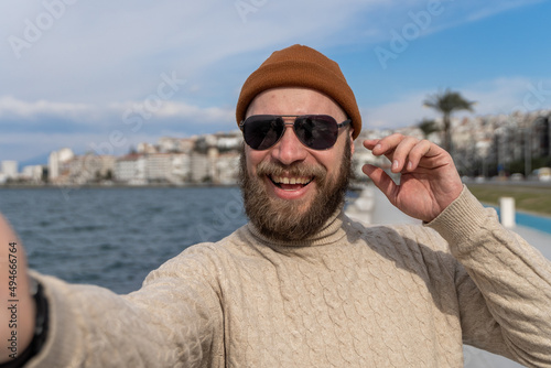 Tourist man taking a selfie while traveling around the sea city in Europe. Happy guy with sunglasses holding smartphone and smiling at camera