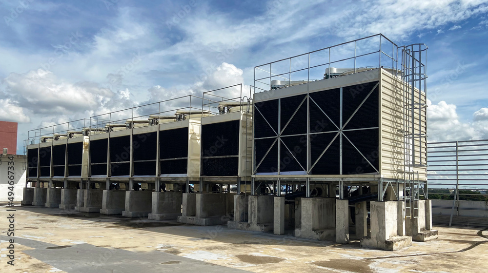 The cooling tower is located in a large data center building installed on the roof on a bright blue sky. And there are white clouds - pictures