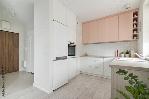 Kuchnia i przedpokój w minimalistycznym nowoczesnym stylu. Białe i różowe fronty mebli oraz sprzęt. Biała lodówka.