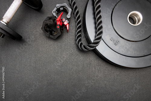 Top down view flat lay with bodybuilding equipment. Barbell, dumbbells, triceps rope and clamps on the floor at the gym on a black background and empty space for text. Fitness, weight training concept