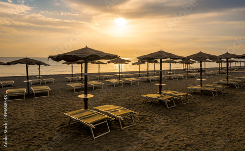  empty beach during beautiful sunrise or sunset with chaise loungues and nice umbrellas with blue sea  sun glow and amazing cloudy sky on thr background