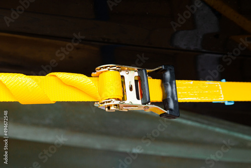 Φωτογραφία Tensioned yellow cargo belt with a ratchet lock on a dark background, close-up