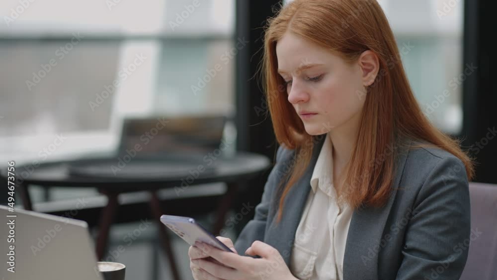 pretty redhead woman in grey jacket is working in co-working area, viewing social media and message in smartphone pretty redhead woman in grey jacket is working in co-working area, viewing social media and message in smartphone