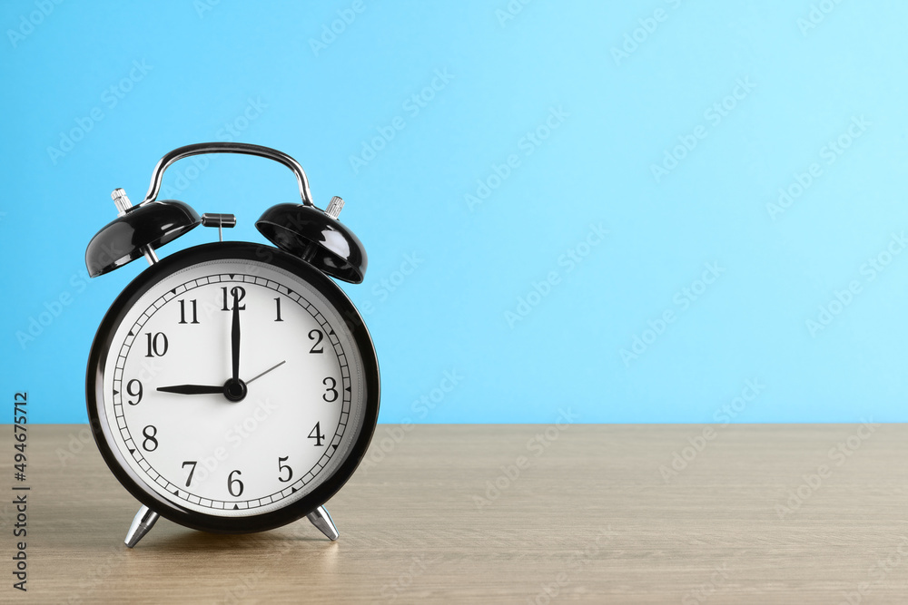 Black alarm clock on wooden table against light blue background, space for text Black alarm clock on wooden table against light blue background, space for text
