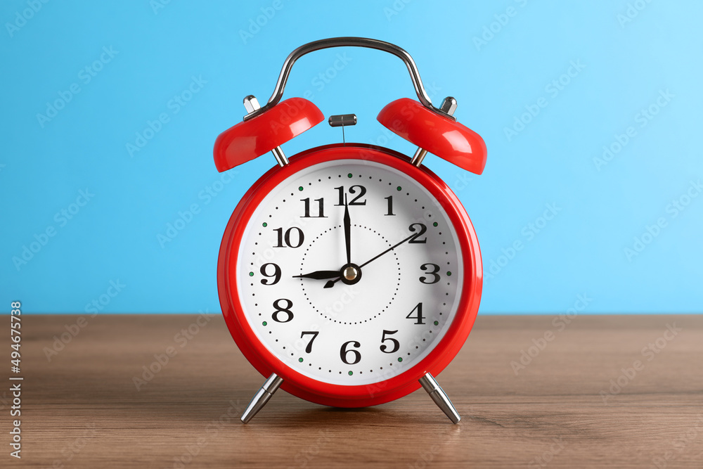 Red alarm clock on wooden table against light blue background Red alarm clock on wooden table against light blue background