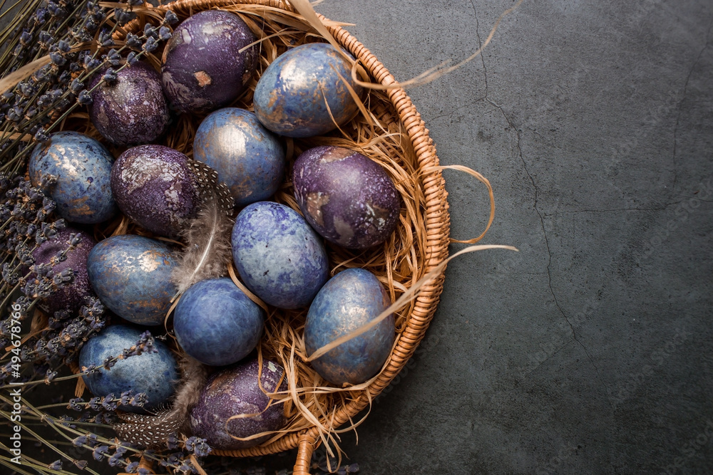 Purple, blue and golden eggs in a basket on a dark background. The purple hue trend of 2022 is very peri. Natural dye karkade tea. Top view. Easter card with a copy of the place for the text. Purple, blue and golden eggs in a basket on a dark background. The purple hue trend of 2022 is very peri. Natural dye karkade tea. Top view. Easter card with a copy of the place for the text.