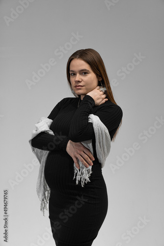 Beautiful pregnant girl of European appearance in a black dress and a white scarf. Portrait of a pregnant girl.