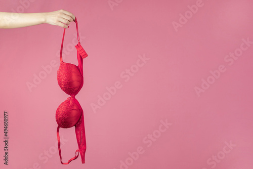 Fototapeta A woman's hand holding a red bra on a pink background