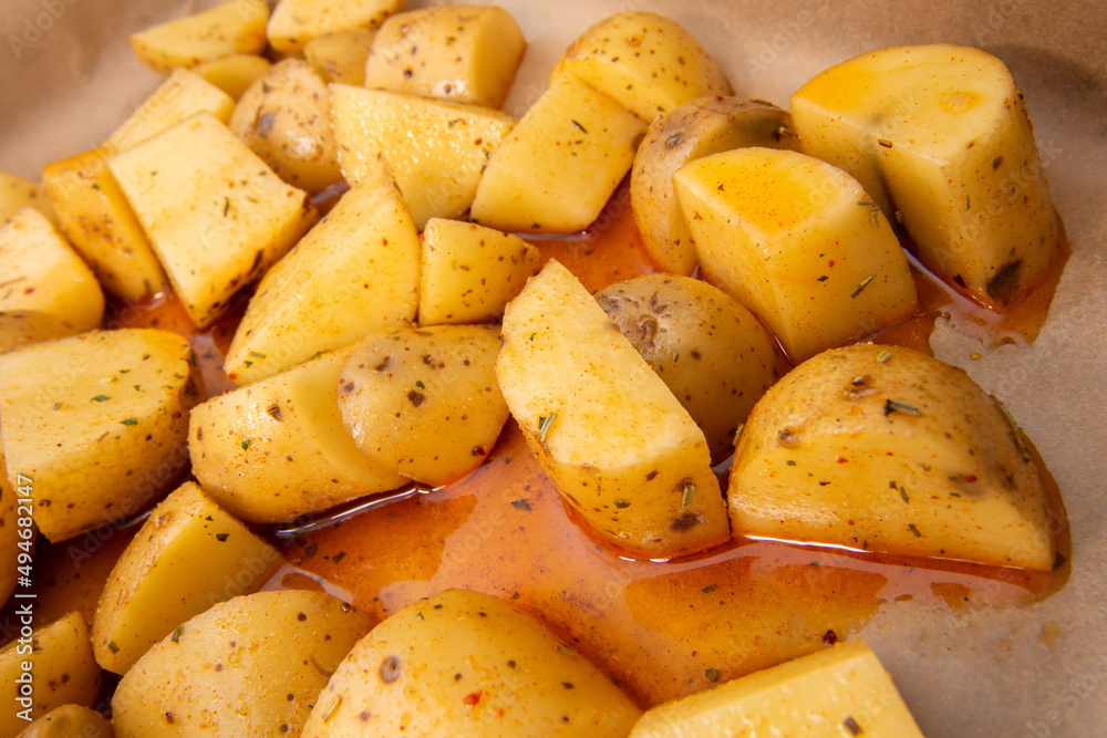 Detail of American potatoes prepared for baking in the oven. chopped fresh potatoes into small pieces and drizzled with oil and spices. Detail of American potatoes prepared for baking in the oven. chopped fresh potatoes into small pieces and drizzled with oil and spices.