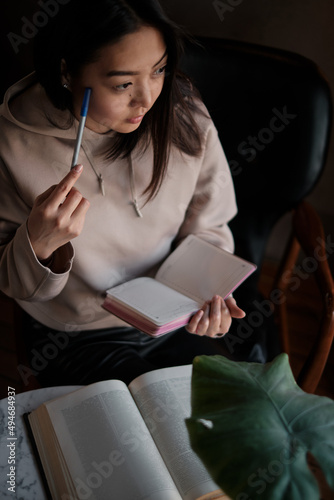 Shot of young asian female student sitting at table and writing on notebook. Young female student studying in cafe.