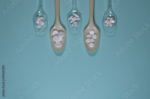 Spoons filled with various pills, on a blue background.