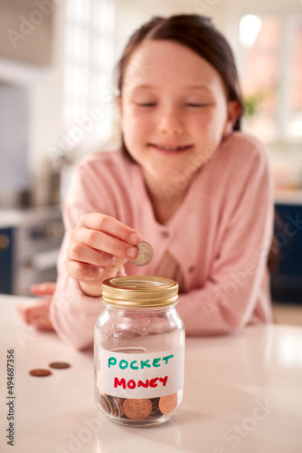 фотографія Girl Saving Money Into Jar Labelled Pocket Money On Kitchen Counter At Home