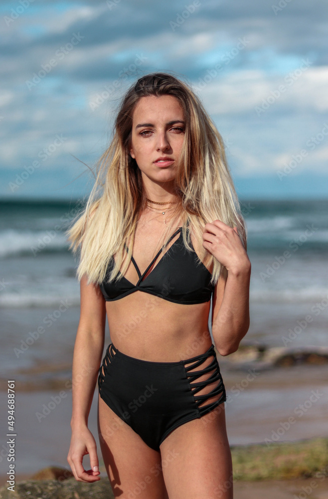 Young, half-bodied blonde woman in high waisted black bikini on the beach