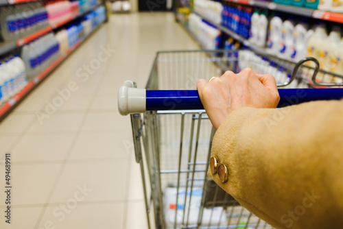 Woman's hand pushing shopping cart in supermarket choosing cleaning products.