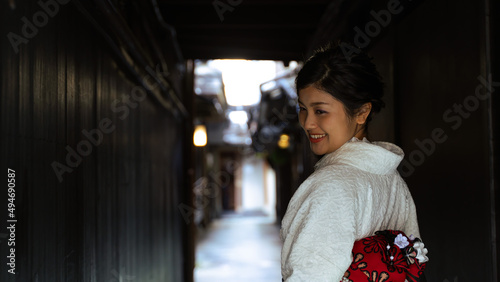 京都、祇園の細い路地で和服を着て笑顔で振り向く日本人女性。バストアップショット