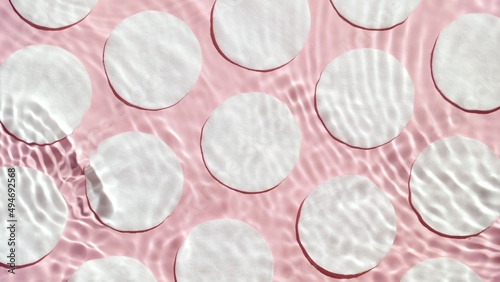 Top view shot of water surface with ripples and spontaneous waves against cotton pads arranged in rows on pale pink background | Background shot for rose water commercial