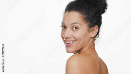 Beauty portrait of young African American woman with curly hair in bun looks at the camera over her shoulder on white background | Beauty care commercial concept