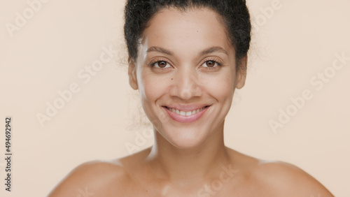 Close-up beauty portrait of young slim African American woman with bare shoulders smiling wide for the camera on beige background   Soft skin concept