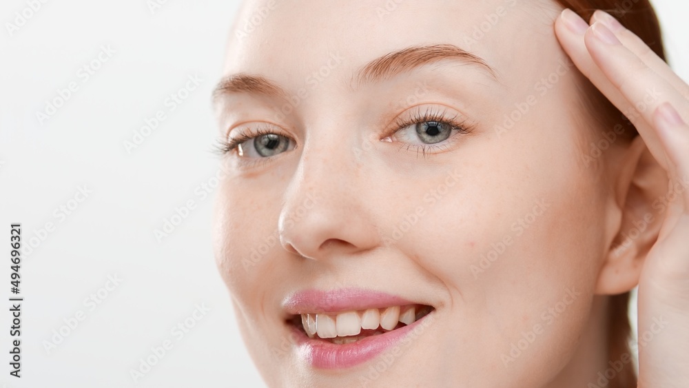 Big close-up shot of good-looking European young red-haired woman touches her face smiling wide for the camera on white background | Skin hydration concept Big close-up shot of good-looking European young red-haired woman touches her face smiling wide for the camera on white background | Skin hydration concept