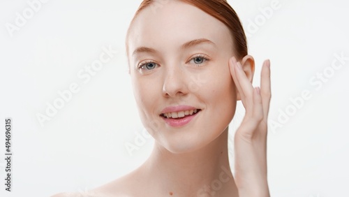 Young positive ginger woman touches her cheek with her finger against light-grey background | Skin care commercial concept