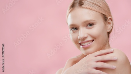 Young fit beautiful Caucasian blonde skin care woman touches her shoulders hugging herself and smiles wide for the camera against pink background with water ripples   Body care lotion commercial