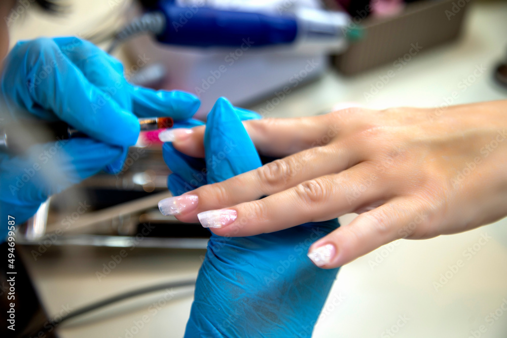 A manicurist places a clear nail extension form to the finger. At a salon or parlor.