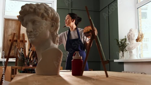 Art studio - young woman drawing a painting - marble bust sculpture on the foreground