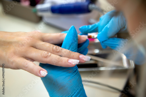 A manicurist places a clear nail extension form to the finger. At a salon or parlor.