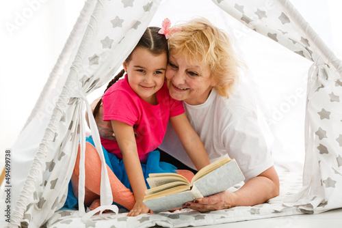 Portrait of happy senior Caucasian woman holding book with little girl in a tent photo