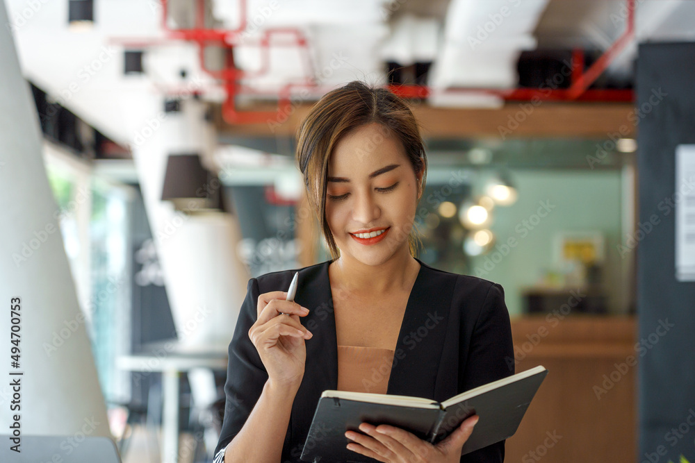Fototapeta premium Smiling beautiful Asian woman writing down notes while standing in the office.