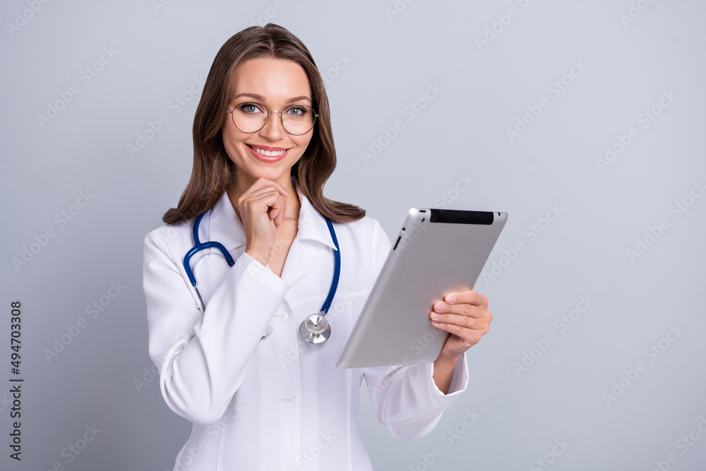 Photo of young cheerful woman family doc lab diagnostic use tablet isolated over grey color background Photo of young cheerful woman family doc lab diagnostic use tablet isolated over grey color background