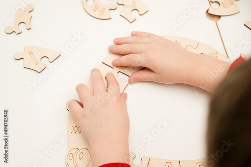 3D wooden toy. Learning letters in order of alphabet. Child's fingers holds pieces of unfinished to assemble puzzle.