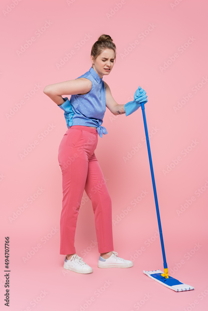 full length of tattooed young woman in rubber gloves holding mop and touching back on pink. full length of tattooed young woman in rubber gloves holding mop and touching back on pink.