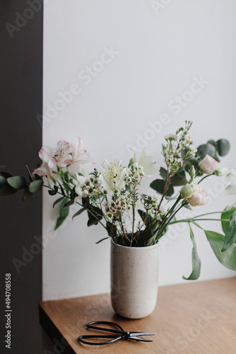 Fototapeta Naklejka Na Ścianę i Meble -  Stylish bouquet in ceramic vase on wooden windowsill. Beautiful fresh flowers and scissors on wooden background, floral arrangement. Spring modern bouquet