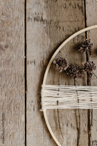 Stylish boho autumn wreath with dry flowers flat lay. Wooden hoop, thread and dry herbs on rustic wooden background. Modern floral arrangement and handmade decor